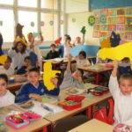 alunni della classe terza b seduti al proprio posto in aula cche alzano la mano facendo vedere una regione dell'italia colorata